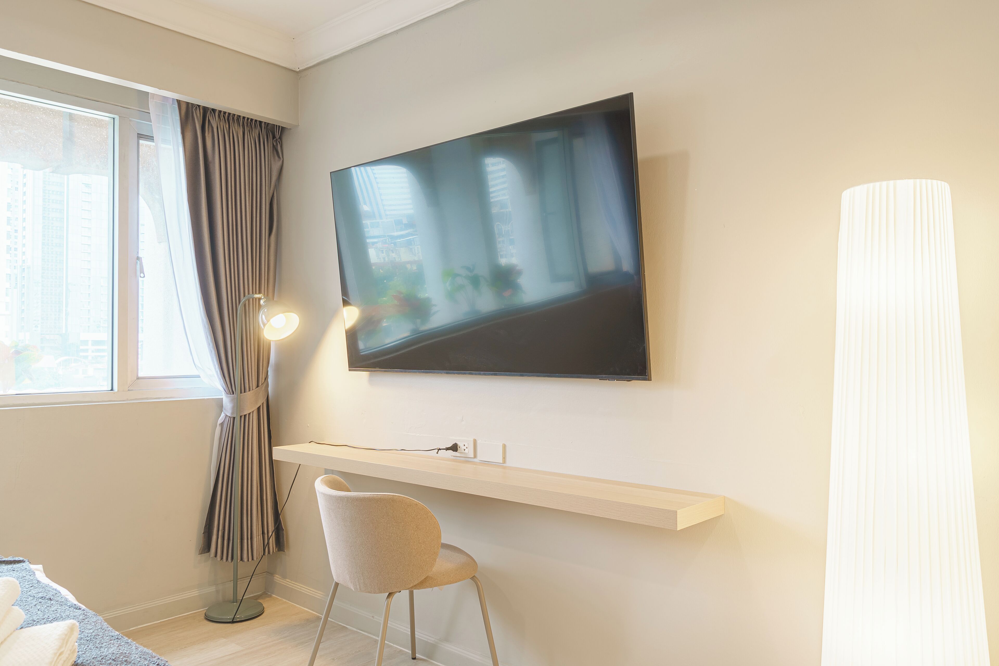 Een moderne hotelkamer met een wandtelevisie, een staande lamp, een stoel en een raam met gordijnen.
