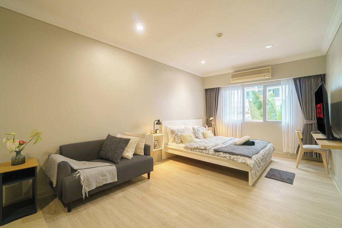 A modern bedroom with a sofa, a bed, a desk, and a TV.