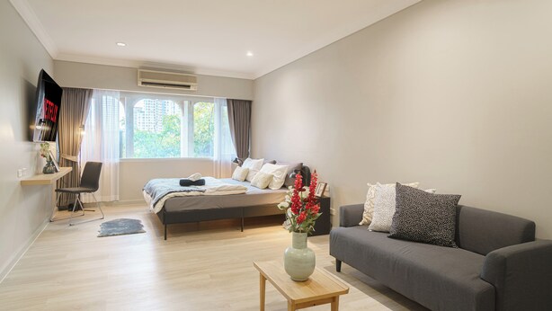 A modern bedroom with a bed, a grey sofa, a wooden coffee table, and a window with curtains. - Casa Amor (Bangkok)