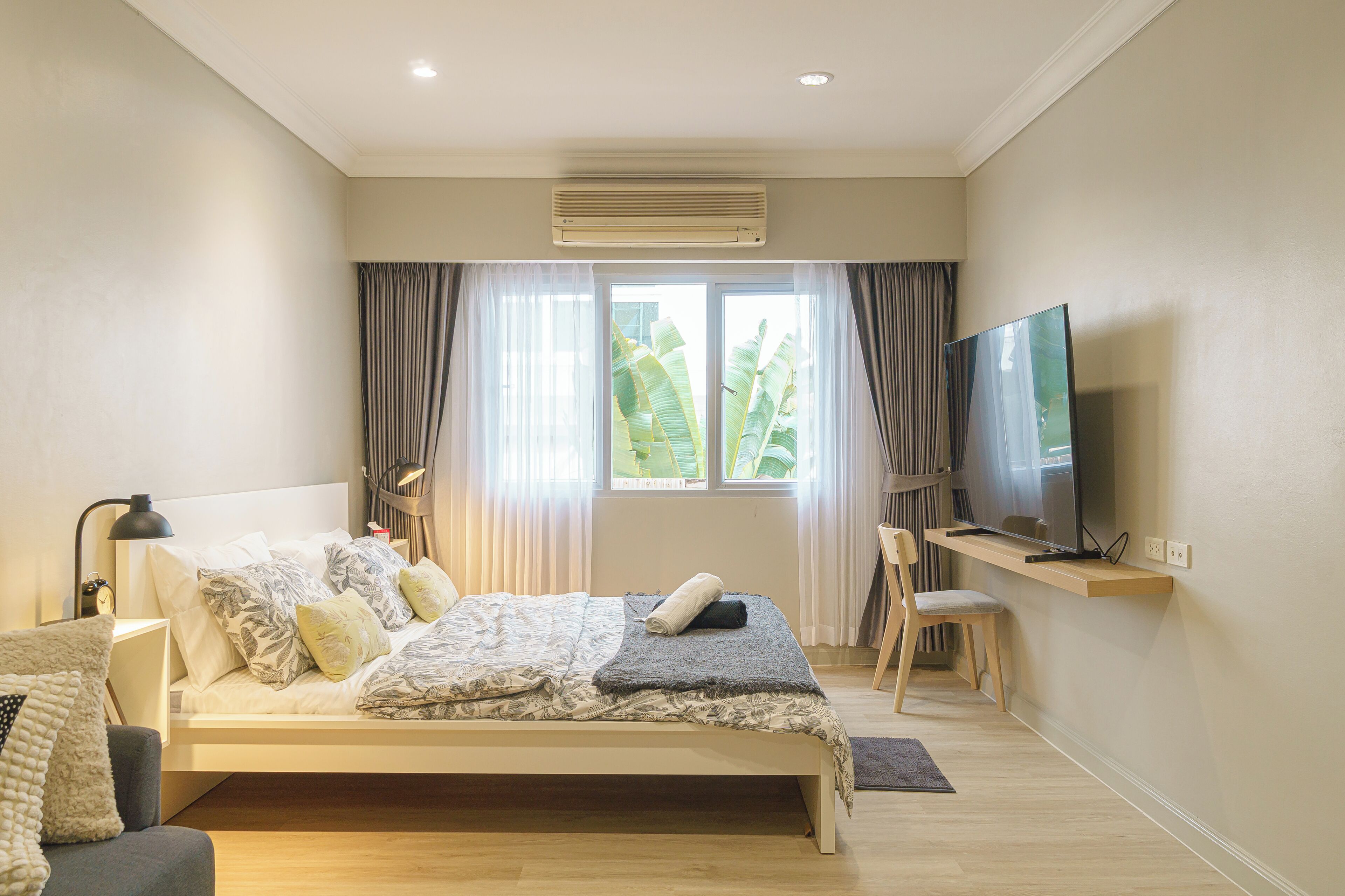 A modern bedroom with a bed, a desk, a chair, a television, and an air conditioning unit.