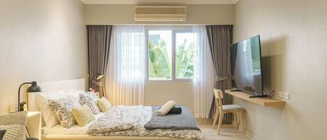 A modern bedroom with a bed, a desk, a chair, a television, and an air conditioning unit.