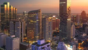 A cityscape at dusk with modern high-rise buildings, including a distinctive skyscraper with a unique architectural design. - Casa Amor (Bangkok)