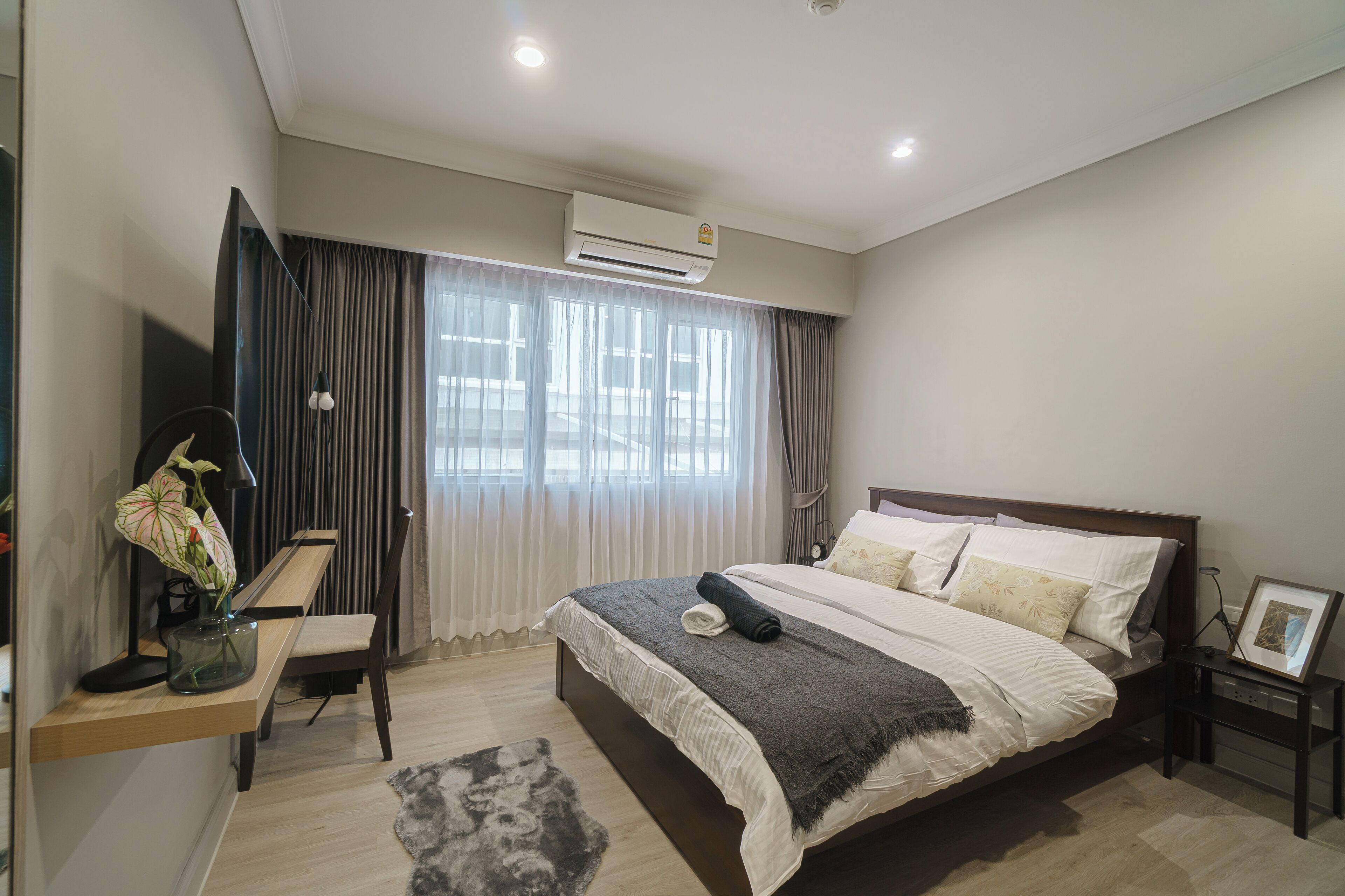 Un dormitorio moderno con una cama grande, un escritorio con silla, un televisor y un equipo de aire acondicionado.