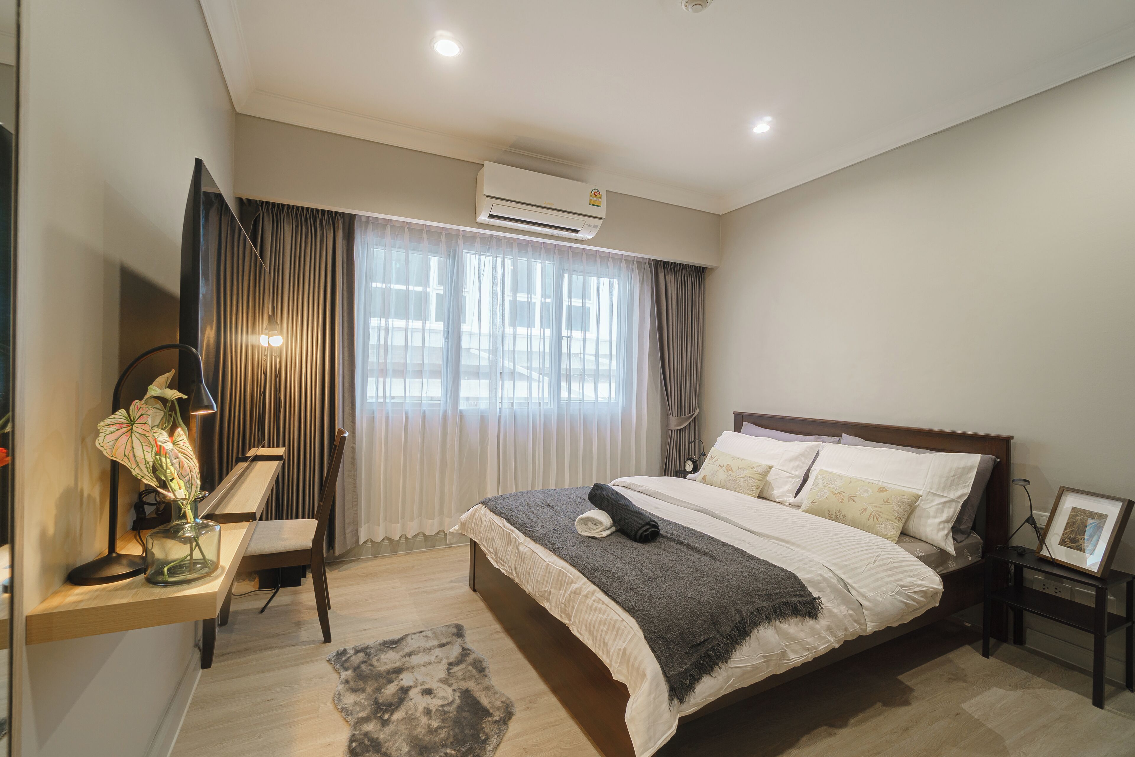 A modern bedroom with a large bed, a desk with a lamp, and a bedside table with a picture frame.