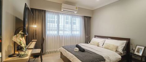 A modern bedroom with a large bed, a desk with a lamp, and a bedside table with a picture frame.