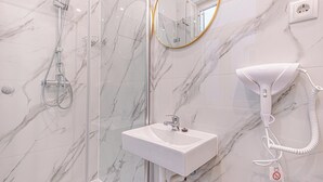 Een badkamer met een marmeren wand, een douche met glazen wanden, een witte wastafel en een aan de muur bevestigde haardroger.