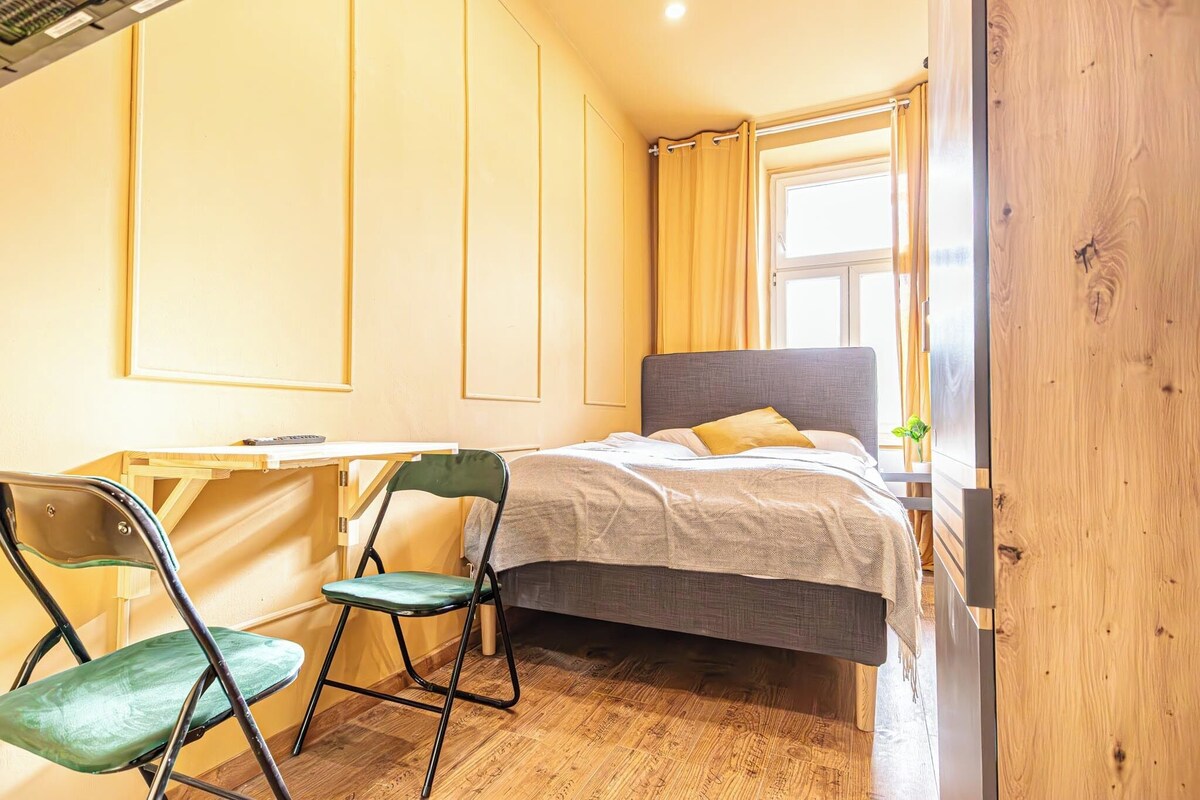Een kleine slaapkamer met een bed, bureau en stoel.