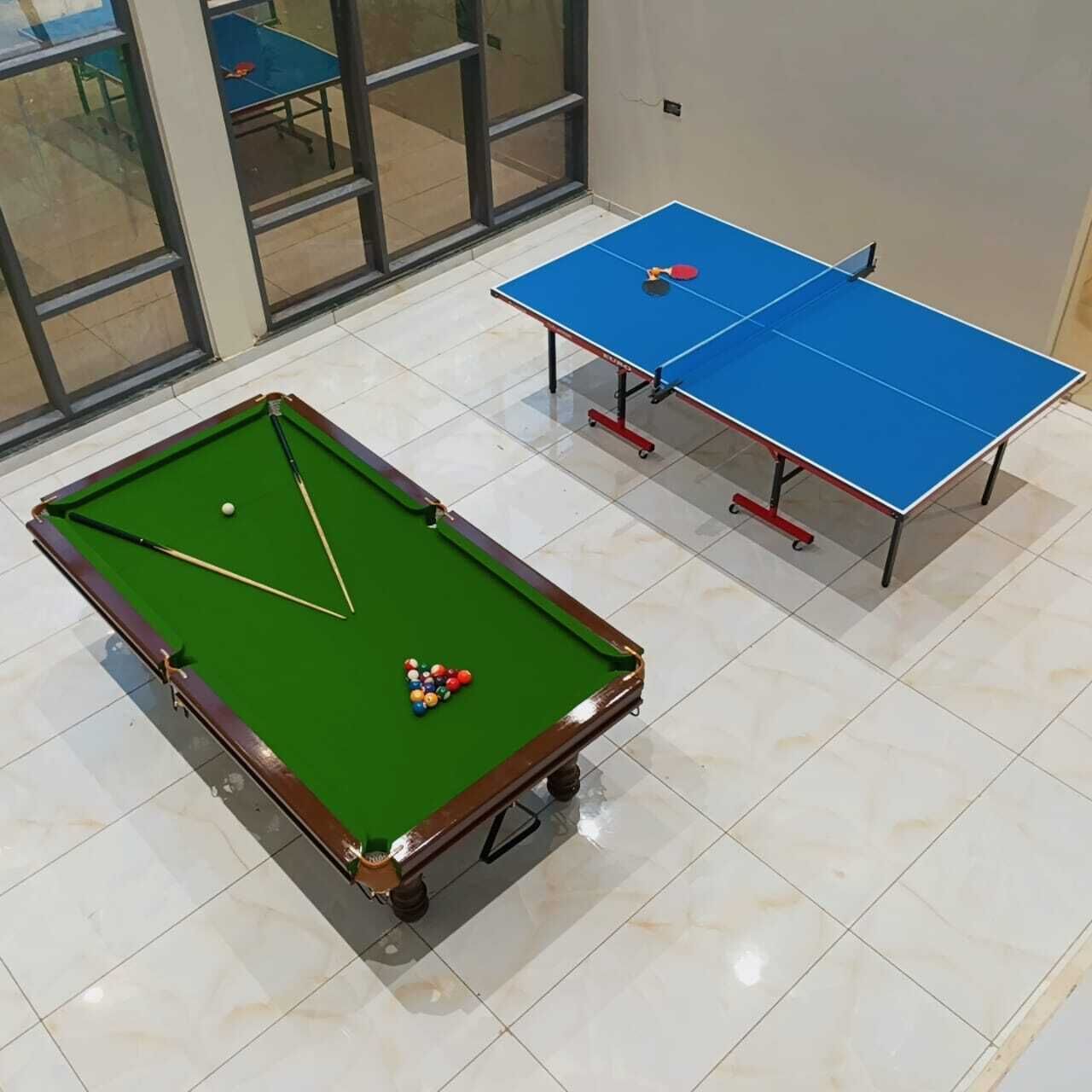 A pool table with balls and cues, a ping pong table, and a billiards table in a room with large windows.