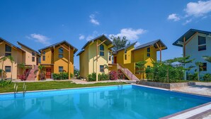 Un espace piscine avec une piscine à l’eau d’un bleu limpide, entourée de bâtiments jaunes dotés de nombreuses fenêtres et d’un escalier menant à l’entrée.