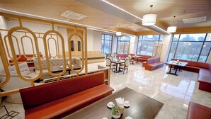 Un hall d’hôtel moderne, doté d’espaces aménagés avec des sièges, d’une table basse ornée d’une plante et de grandes fenêtres offrant une vue panoramique.