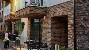 A building with a sign reading "All Seasons." It features a brick facade, large windows, and outdoor seating with a bench. - All Seasons Palanga (Palanga)