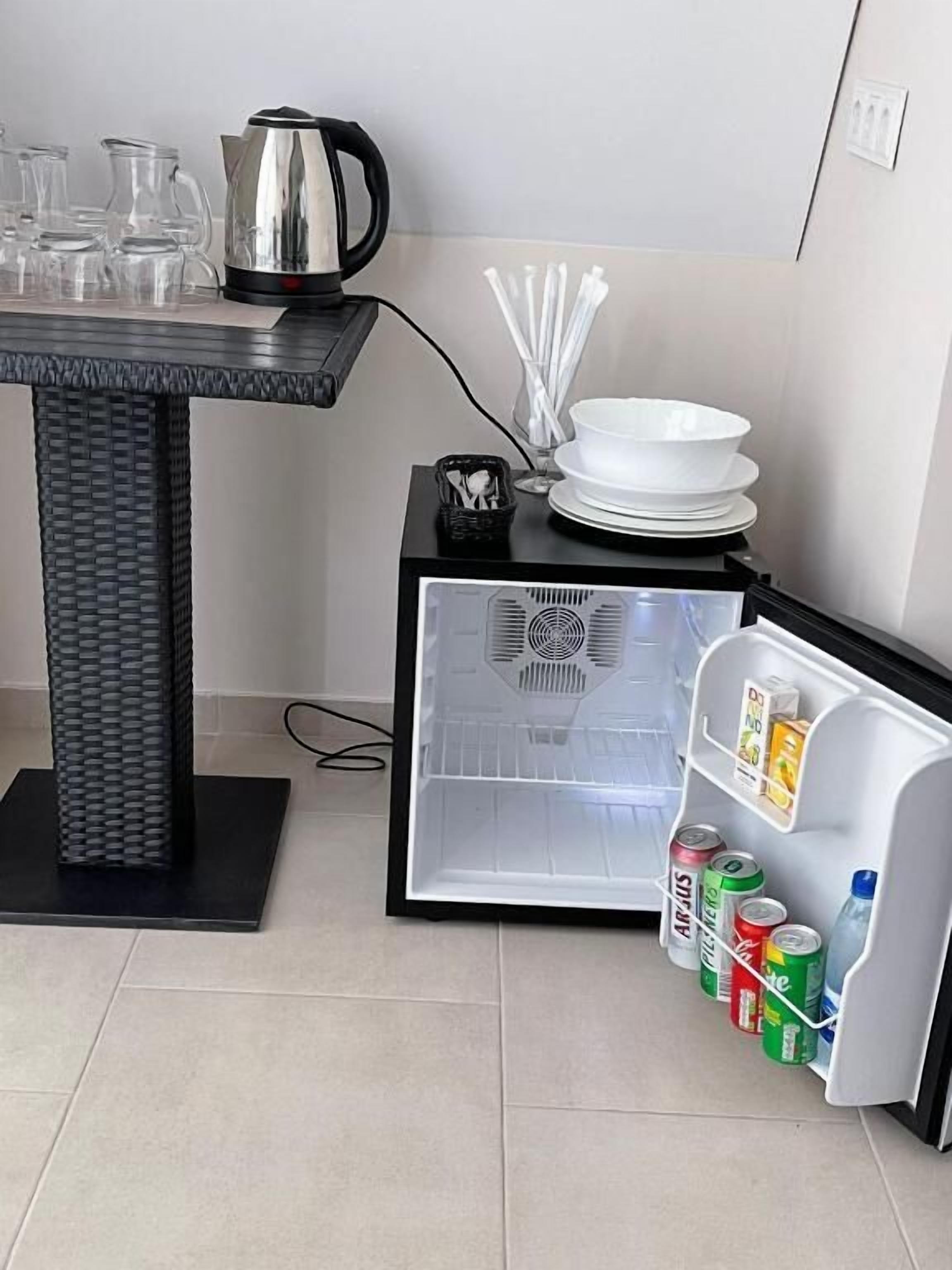 A compact kitchen area with a refrigerator, a small table with a kettle, and a few glass containers.