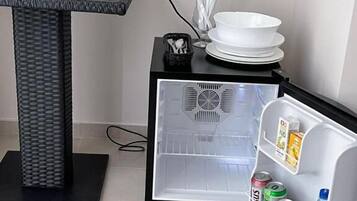 A compact kitchen area with a refrigerator, a small table with a kettle, and a few glass containers.