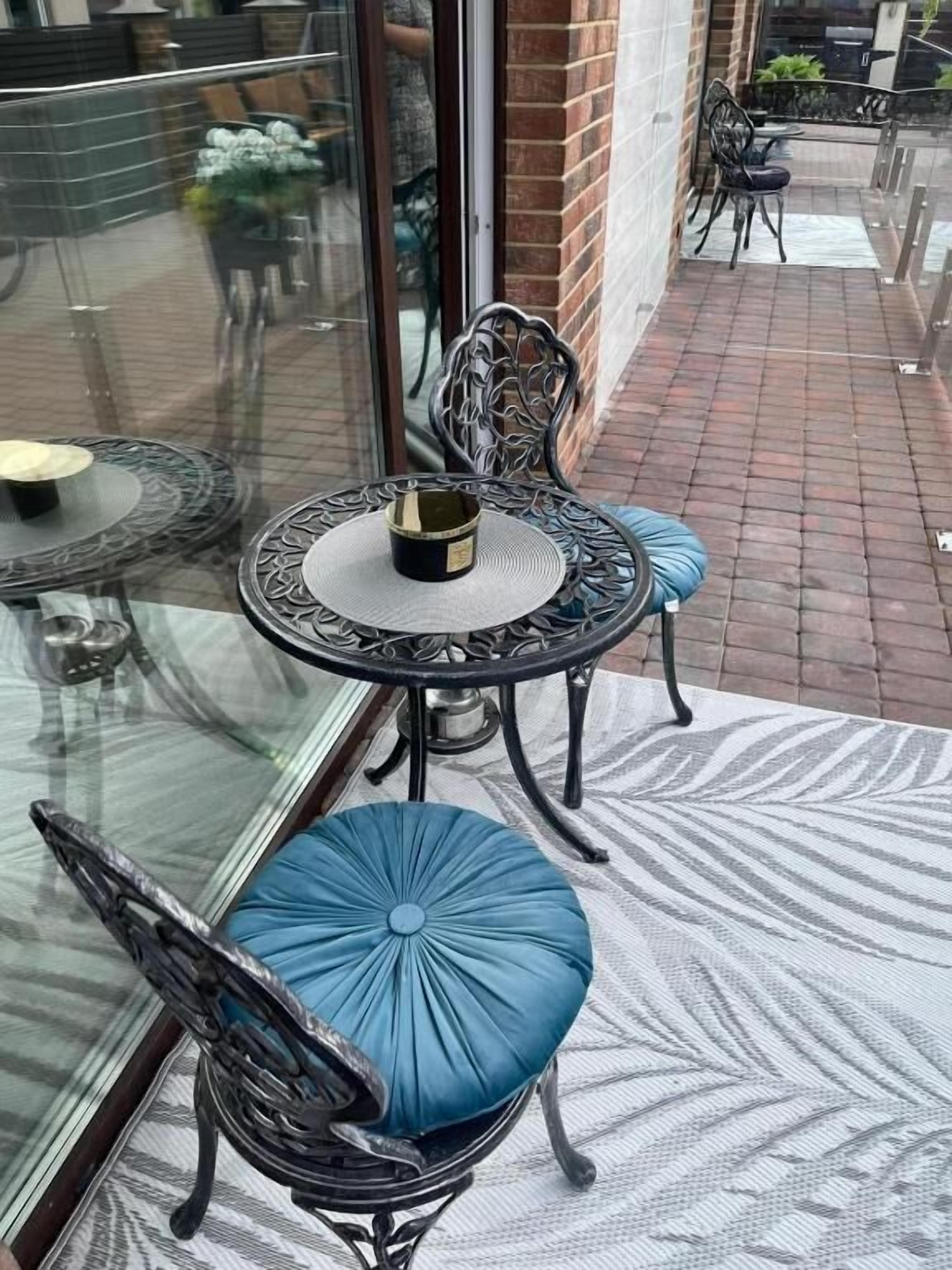 A glass-enclosed balcony with a round table and two chairs, one with a blue cushion.