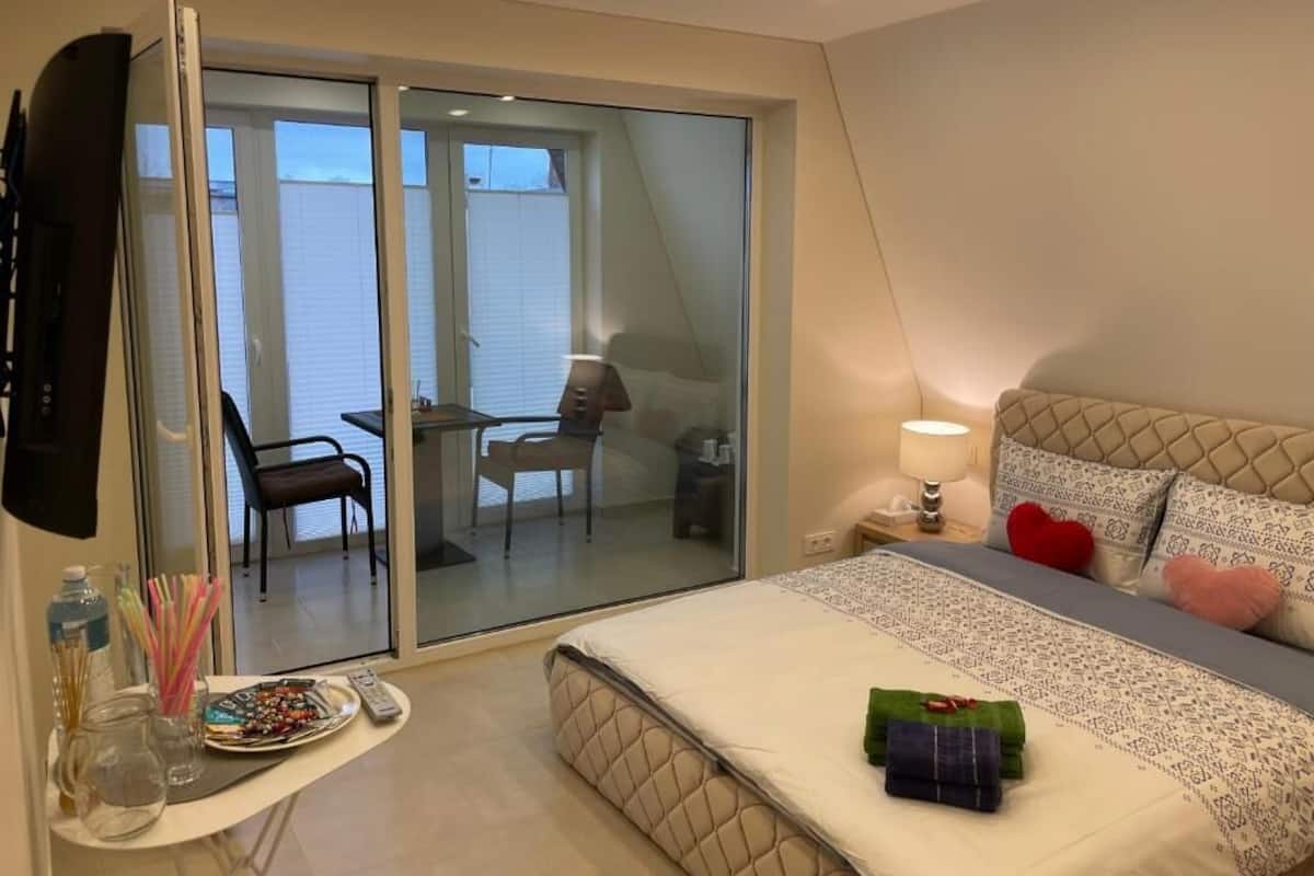 A bedroom with a bed, a bedside table, a lamp, a TV, and a sliding glass door leading to a balcony.