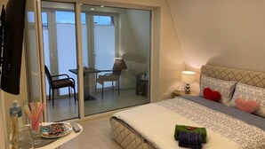 A bedroom with a bed, a bedside table, a lamp, a TV, and a sliding glass door leading to a balcony. - All Seasons Palanga (Palanga)