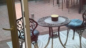 A room with a sliding glass door leading to an outdoor patio area. The patio features a round table with chairs, a patterned rug, and a small decorative bowl. - All Seasons Palanga (Palanga)