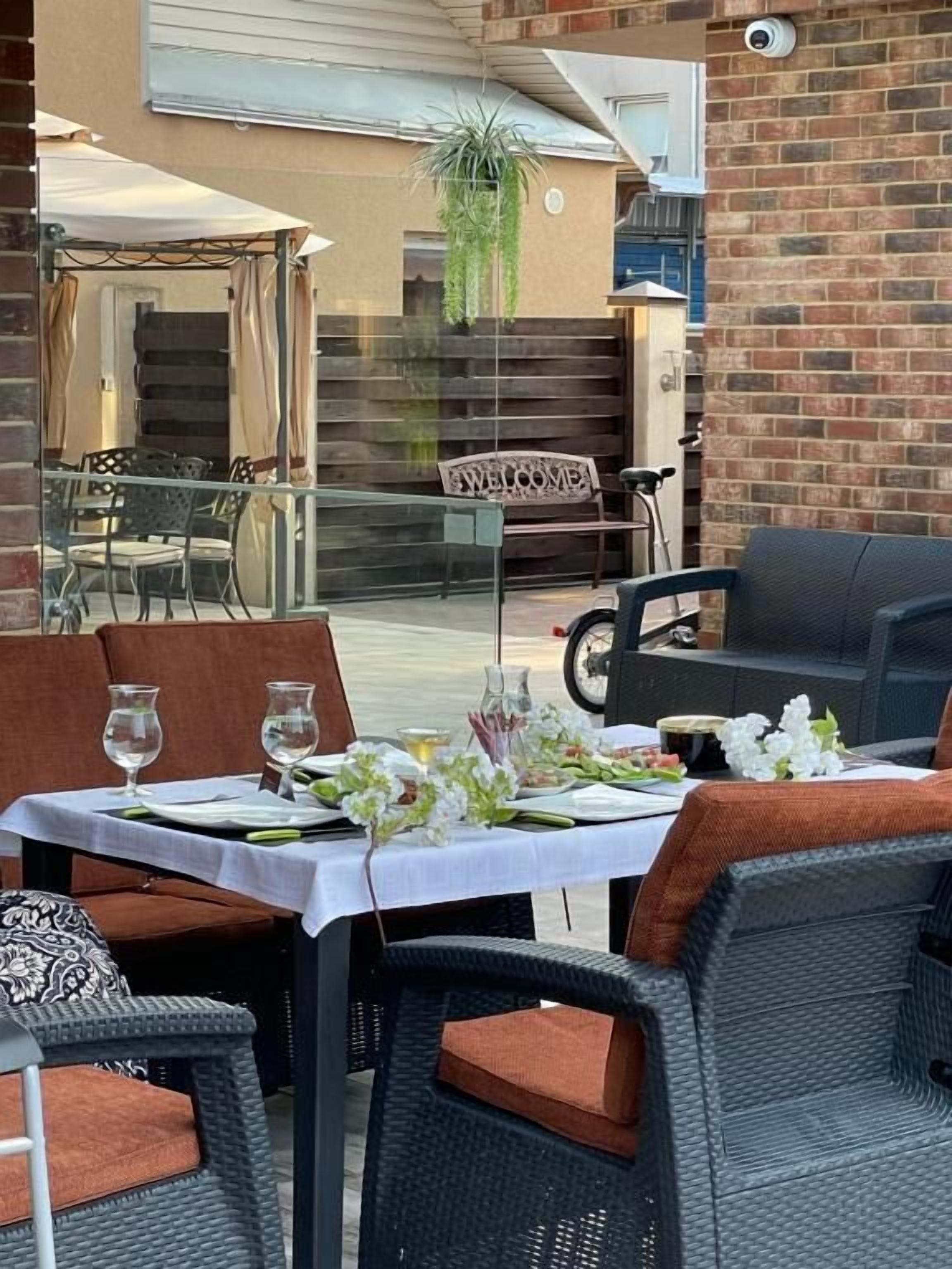 Un área de comedor al aire libre con mobiliario de mimbre y una mesa para dos, con mantel blanco y centros de mesa florales.