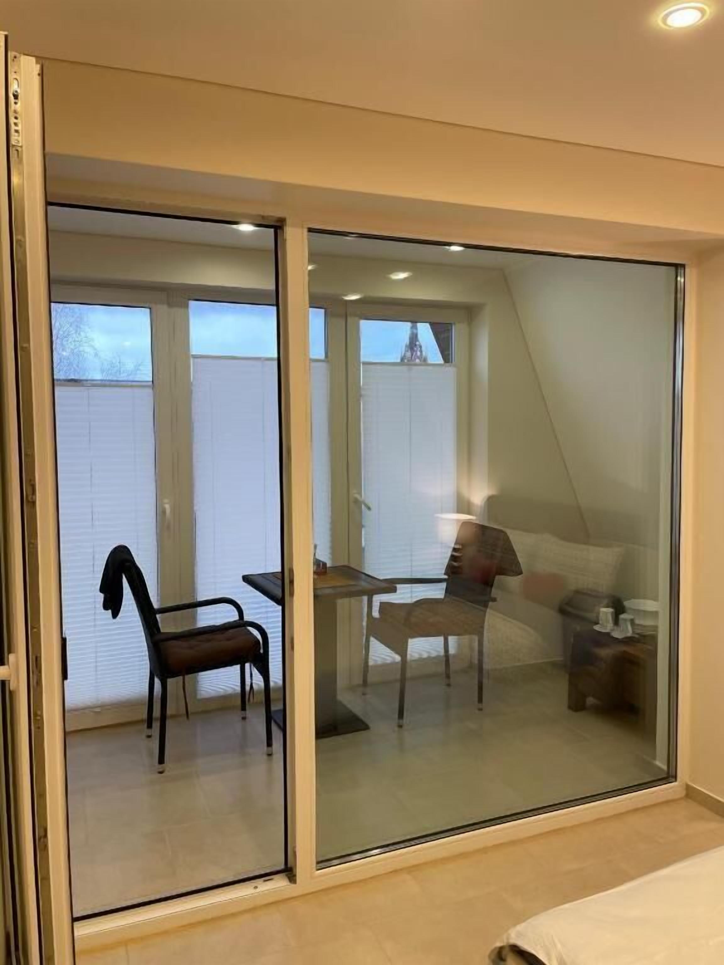 Un dormitori amb una porta corredissa de vidre que dona a un balcó. A la habitació hi ha un llit, una tauleta de nit i una cadira.