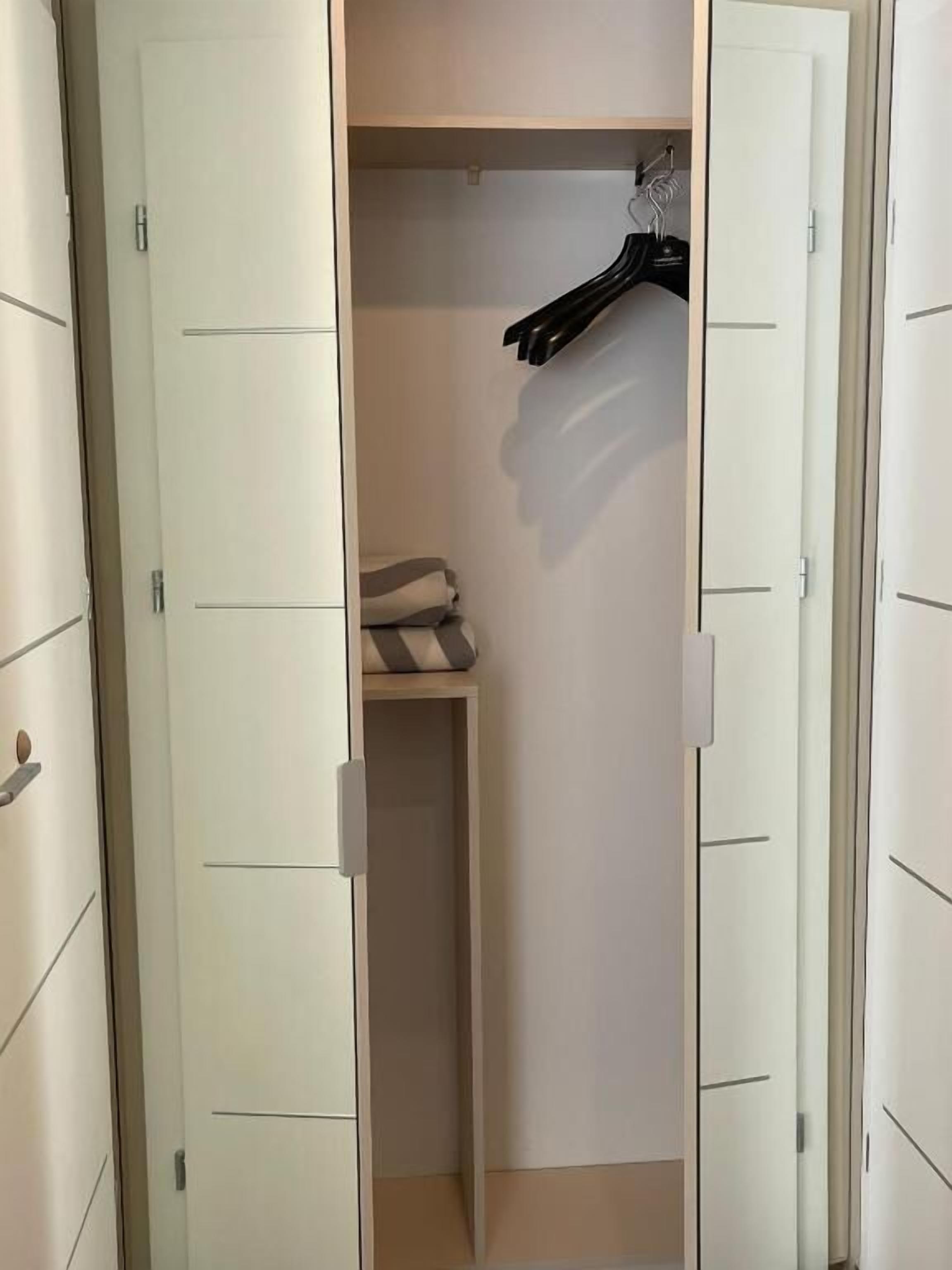 A walk-in closet with white doors, a hanging rack, and folded towels.