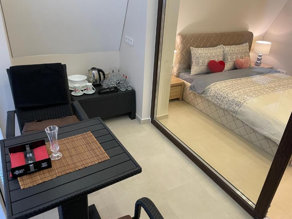 A compact hotel room with a bed, bedside table, and a small table with a glass and a box.