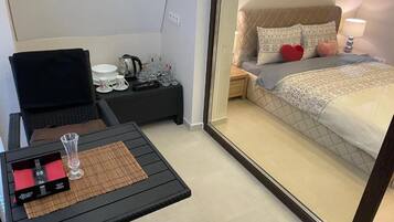 A compact hotel room with a bed, bedside table, and a small table with a glass and a box.