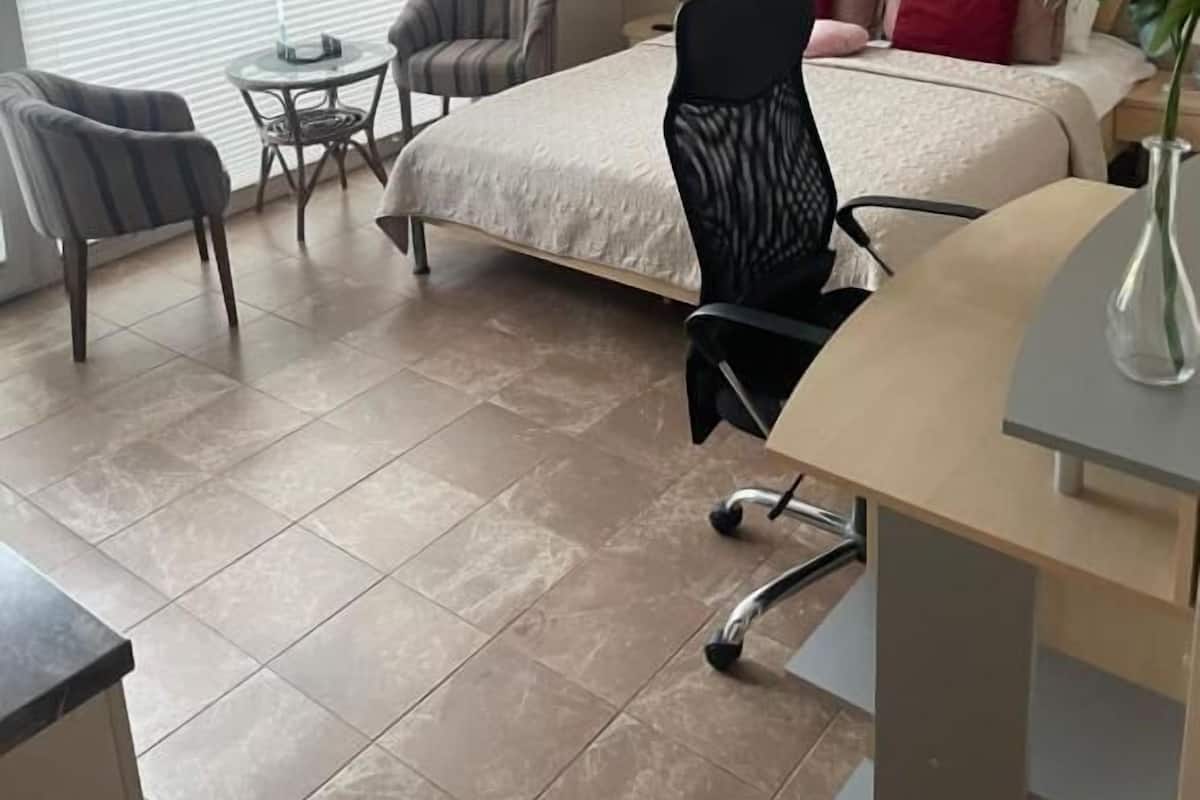 A bedroom with a bed, a desk, a chair, a small table, and a window.