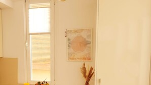 Une cuisine avec un réfrigérateur blanc, deux chaises en osier, une petite table avec des fruits et un tableau accroché au mur.
