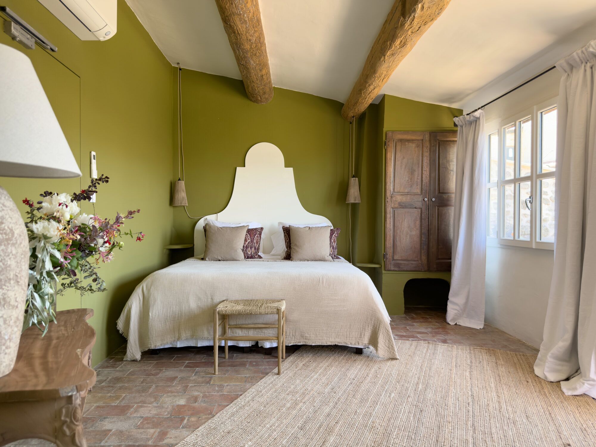 Een slaapkamer met een bed, een nachtkastje, een houten stoel, een geweven vloerkleed en een houten kledingkast.