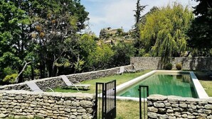 A swimming pool surrounded by stone walls and lush greenery, with a clear blue sky above. - Auberge du Presbytère (Saignon)