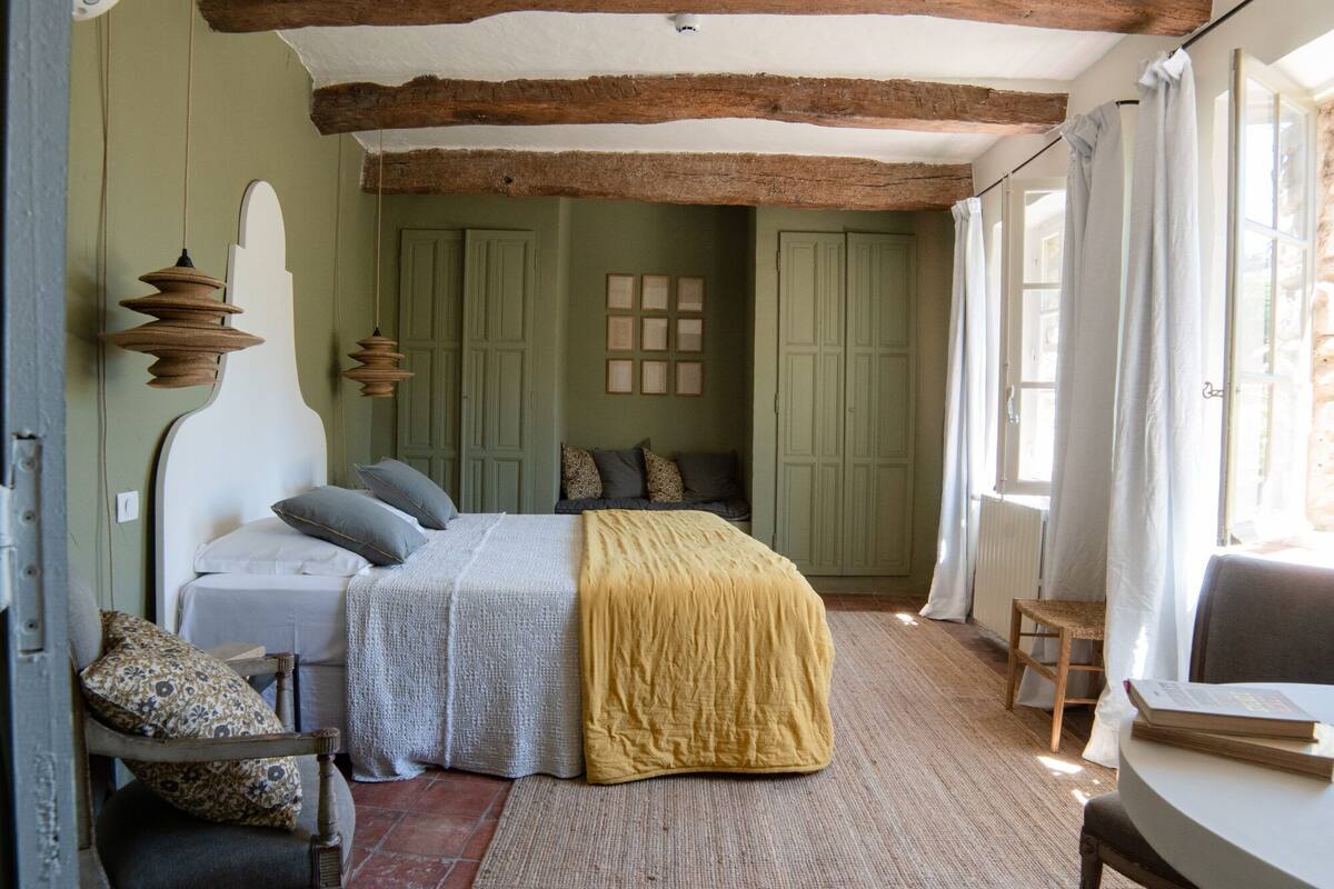 A bedroom with a bed, a chair, a table, and a window.
