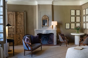 Quarto com lareira, obras de arte emolduradas na parede e uma mesa redonda com um vaso.