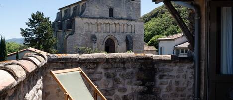 A stone wall with a wooden chair and a small table, a stone building with a bell tower, and a clear sky.