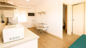 A compact kitchen with a microwave, a small table, and a chair. There is a TV mounted on the wall and a door leading to another room. - El Palmar Family Hideaway Near the Sea (Vejer de la Frontera)
