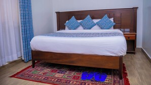 Ein ordentlich bezogenes Bett mit einem Holzkopfteil, einem gemusterten Teppich und einem Paar blauer Hausschuhe auf dem Boden.