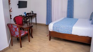 Ein Hotelzimmer mit Bett, Schreibtisch, Stuhl, Fernseher und Vorhängen.