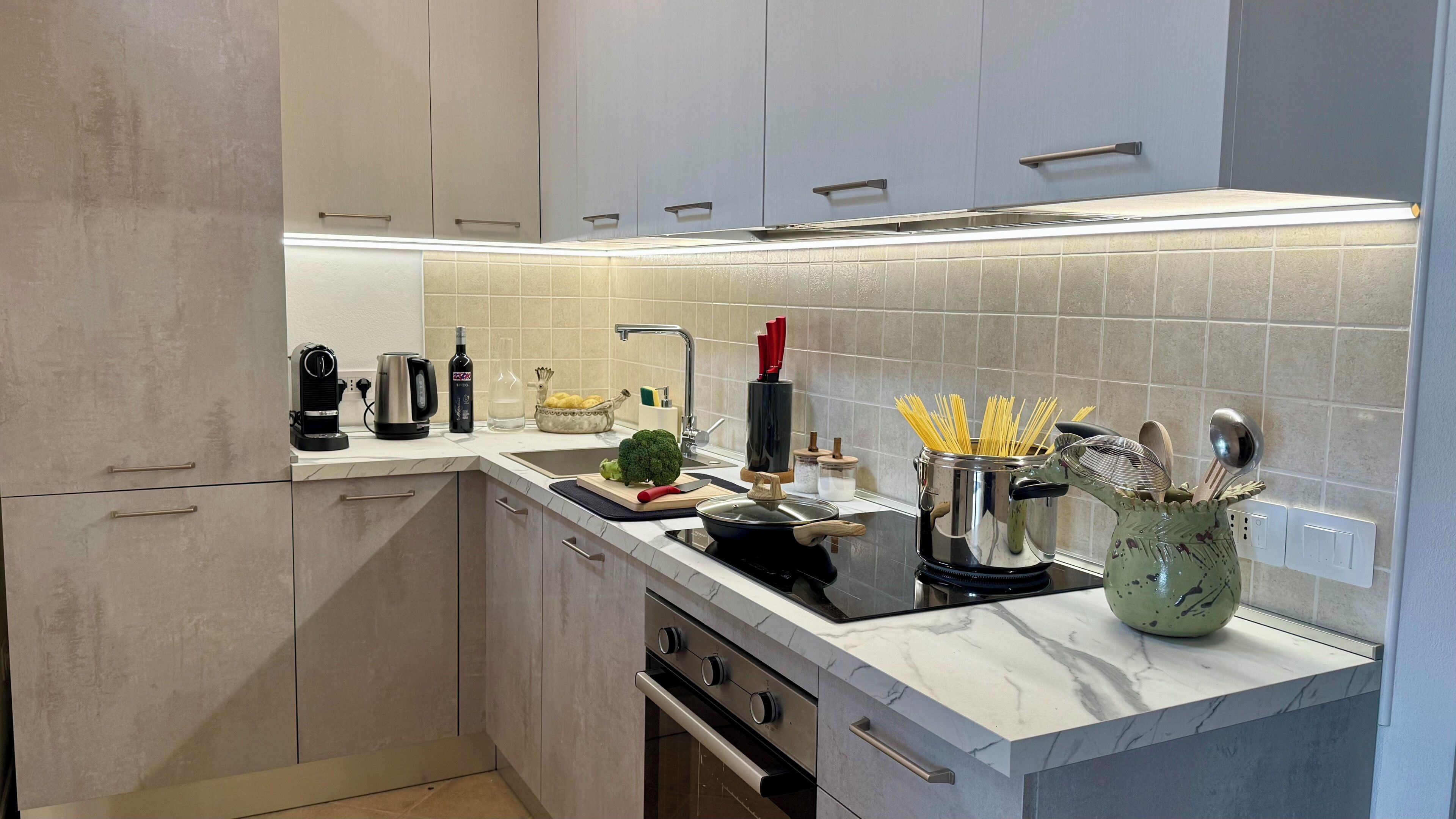 A modern kitchen with a built-in stove, a sink, and a countertop with various kitchen items.