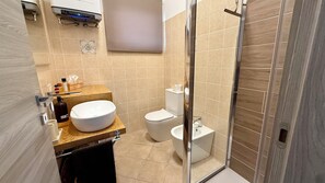Une salle de bain équipée de toilettes, d’un bidet et d’un grand lavabo installé sur un plan de toilette en bois.