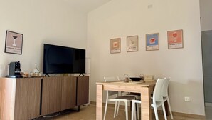 A modern living room with a TV, a coffee machine, a dining table with chairs, and wall-mounted framed pictures. - Sweet Holidays (Magomadas)