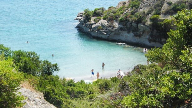 A coastal area with clear blue water, rocky cliffs, and lush greenery. - Sweet Holidays (Magomadas)