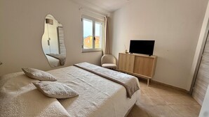 A bedroom with a bed, a mirror, a chair, a TV, and a window. - Sweet Holidays (Magomadas)