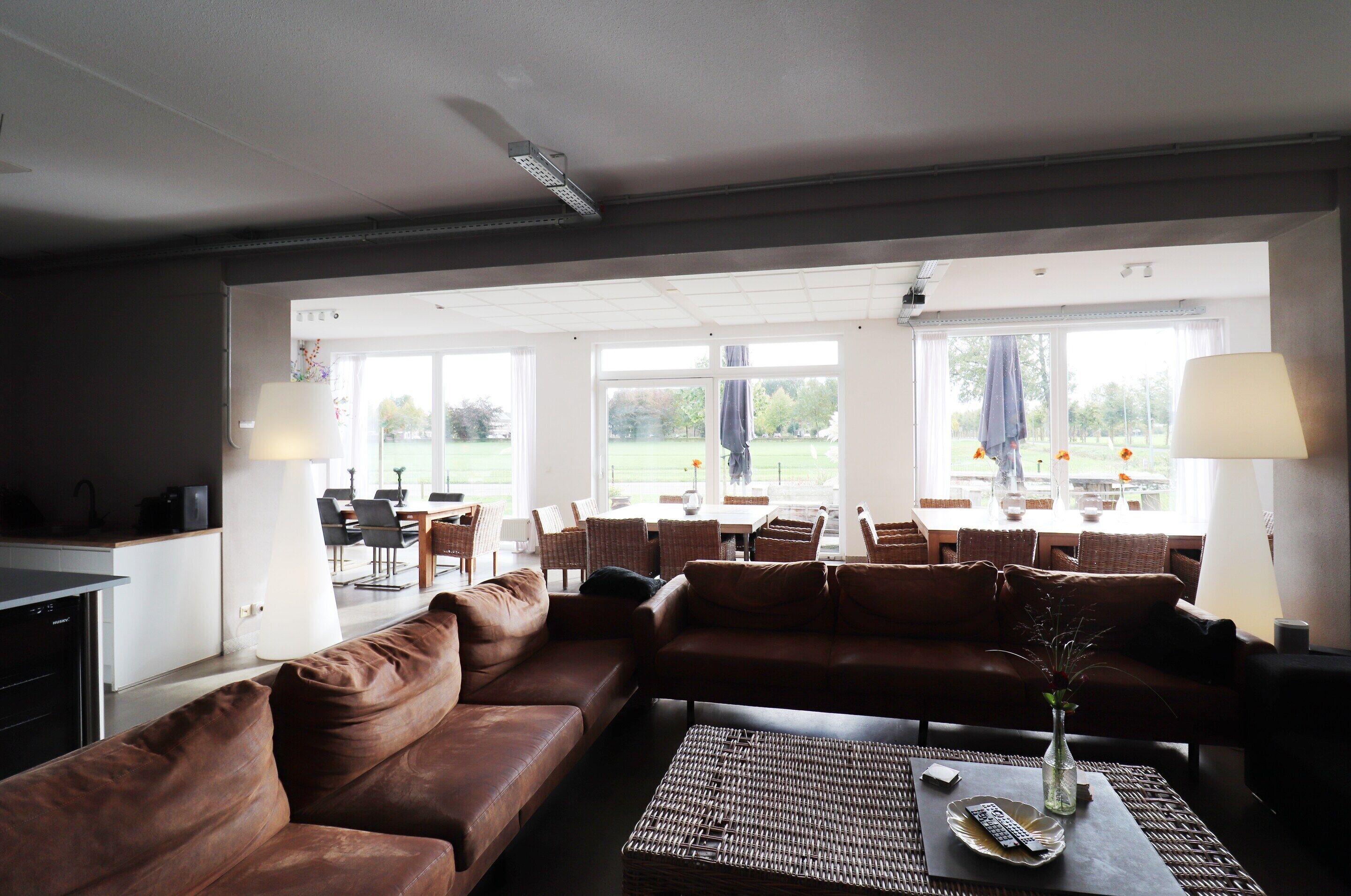 A spacious living area with a brown leather sofa, a wicker coffee table, and a dining area with chairs and a table.