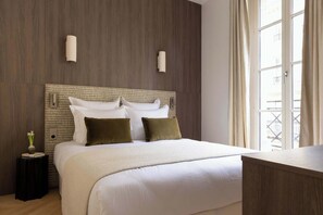 Hotelkamer met een groot bed, nachtkastje, een wandlamp en een raam met gordijnen.