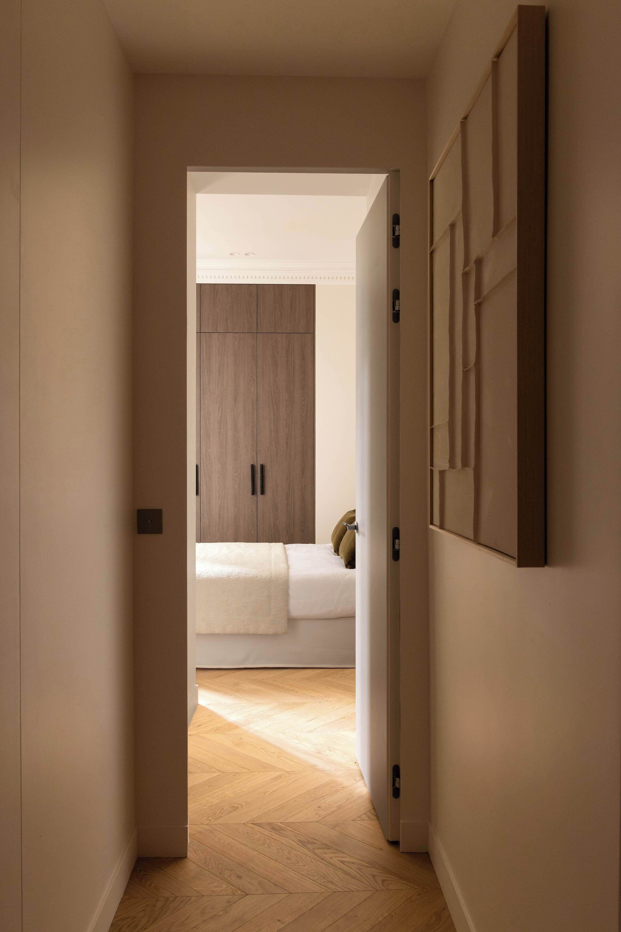 Ein Flur, der in ein Schlafzimmer mit Bett, Kleiderschrank und Wandpaneel führt.