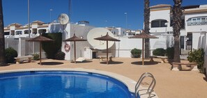 Un espace piscine avec une piscine à l’eau cristalline, des parasols et des chaises longues.