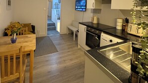 Uma cozinha moderna com piso de madeira, um espaço de refeições com mesa e cadeiras, e uma TV fixada na parede.