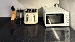 Uma cozinha compacta com armários brancos, bancada preta, torradeira, micro-ondas e diversos utensílios de cozinha.