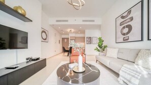 A modern living room with a flat-screen TV, a marble coffee table, a sofa, and a dining area in the background. - Oshima Act Two Downtown 1BR Burj Khalifa (Dubai)