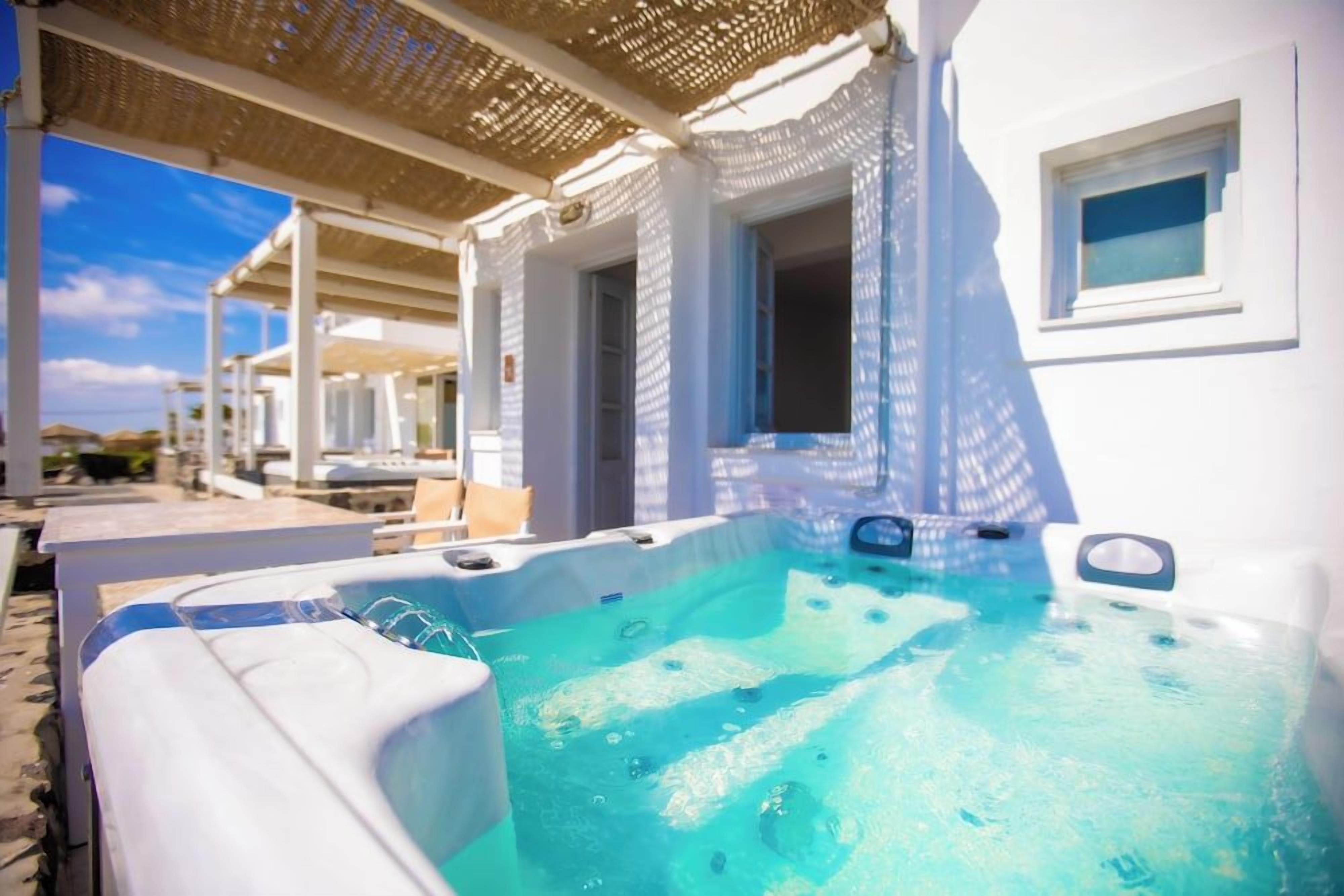 A hot tub area with a pergola overhead, a poolside lounge, and a view of the sea.