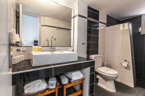A modern bathroom with a large mirror, white sink, and toilet. - Rhapsody Traditional Apartments (Santorini)